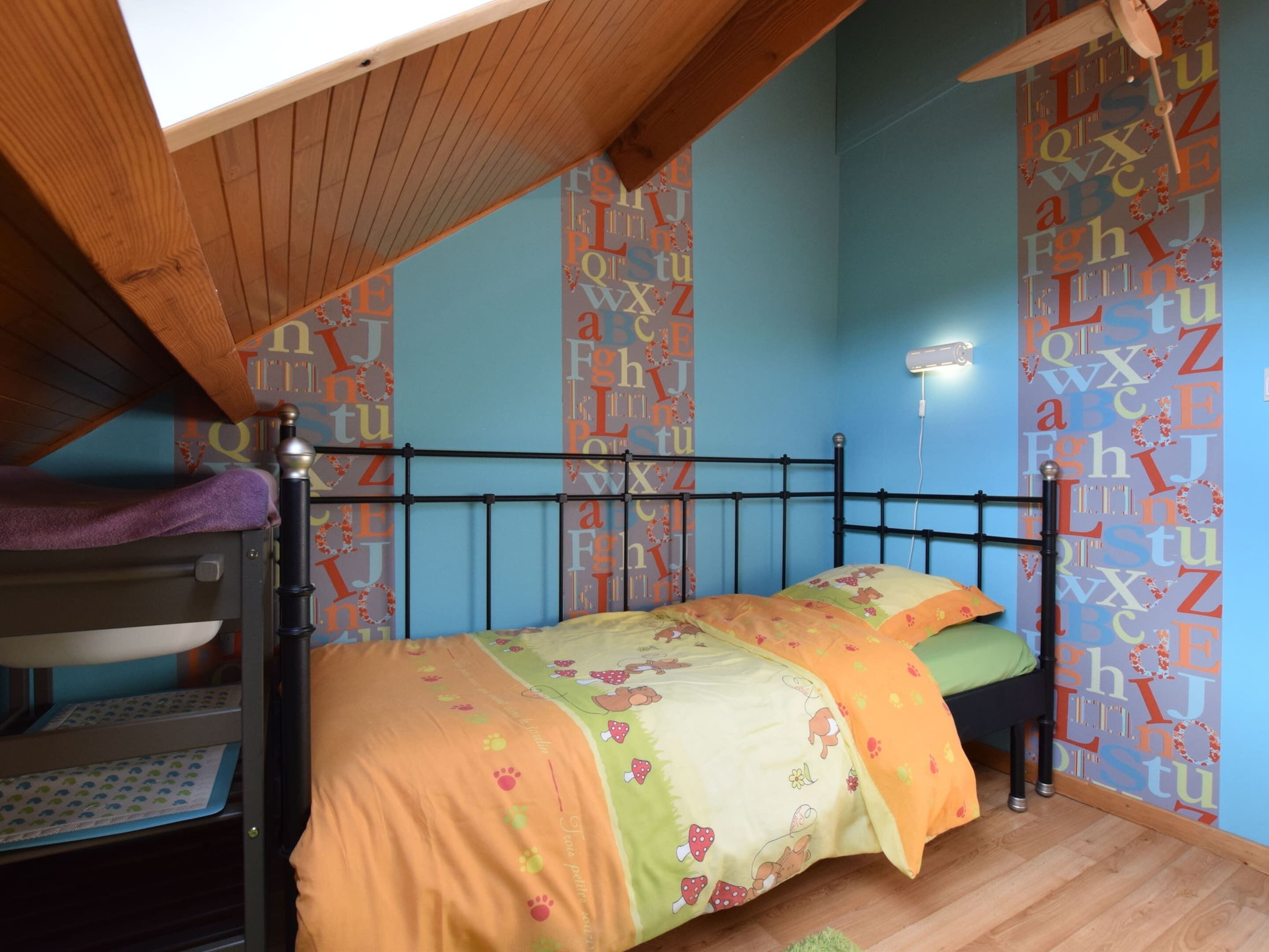 Ein Schlafsaalzimmer mit Etagenbetten, einem Deckenventilator und Wandpapier mit Alphabet-Motiven.