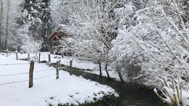 Un paysage enneigé avec une structure en bois, une clôture et un ruisseau.