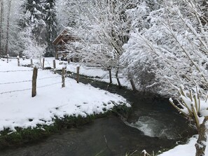 Un paysage enneigé avec une structure en bois, une clôture et un ruisseau.