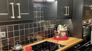 Une cuisine moderne avec des meubles noirs, un plan de travail en bois, une cuisinière encastrée et un four en acier inoxydable.