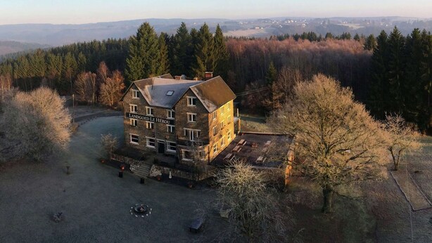 A two-story stone building with a sign reading "Landgoed Le Hérou" surrounded by a forested landscape. - Beautiful Country House in the Ardennes With Lots of Privacy (La Roche-en-Ardenne)