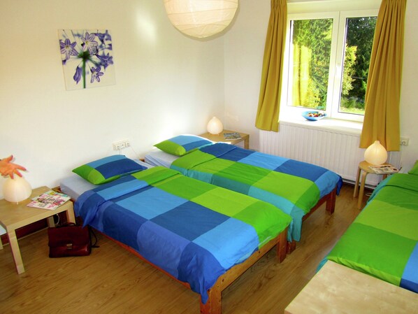 A bedroom with two beds, a nightstand, a lamp, a window with curtains, and a wall art piece.