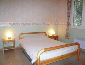 Ein Schlafzimmer mit einem hölzernen Bett, zwei Nachttischlampen, einem blumigen Bordürenmuster und einem Fenster mit Vorhang.