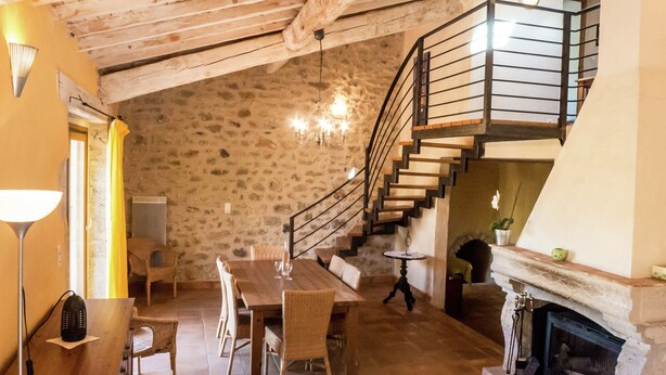 Een rustiek interieur met een eethoek, trap en open haard.