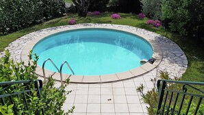 A circular swimming pool with a stone border, surrounded by a tiled patio, and a metal railing on one side. - New Villa, Round Swimmingpool, Beautiful View (Saint-Laurent-de-Carnols)