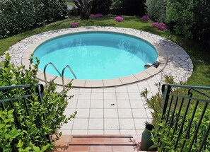 A circular swimming pool with a stone border, surrounded by a tiled patio, and a metal railing on one side. - New Villa, Round Swimmingpool, Beautiful View (Saint-Laurent-de-Carnols)