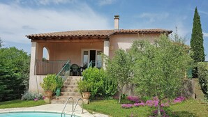 A house with a swimming pool, a covered patio, and a garden with various plants and flowers. - New Villa, Round Swimmingpool, Beautiful View (Saint-Laurent-de-Carnols)