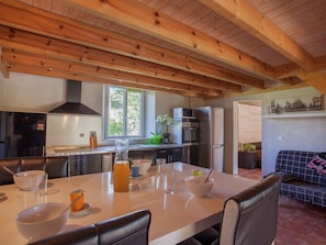 A modern kitchen with wooden beams, a dining table with chairs, a refrigerator, and a window with a view. - Apartment in Corsica Near Beaches (Poggio-Mezzana)