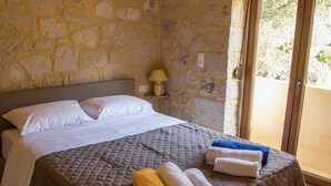 Un llit amb un edredó marró acolxat, almoines blanques i tovalloles enrotllades de groc i blanc. Una làmpada hi ha sobre una tauleta de nit al costat del llit.