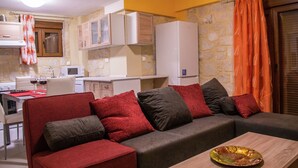 Un espai vital compacte amb sofà, taula de dinar, zona de cuina i paret de pedra.