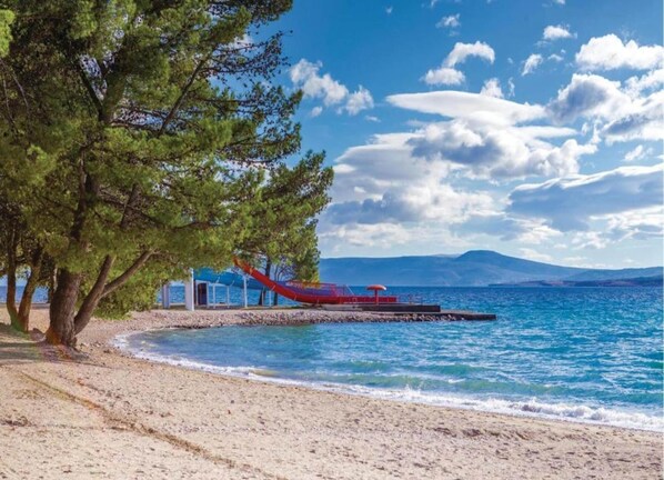 Une plage avec un bateau rouge, des arbres et un ciel dégagé.