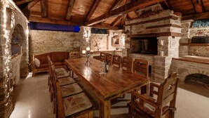 A rustic dining area with a wooden table and chairs, stone walls, and a stone fireplace. - Villa in Murter Near Kornati National Park (Murter-Kornati)