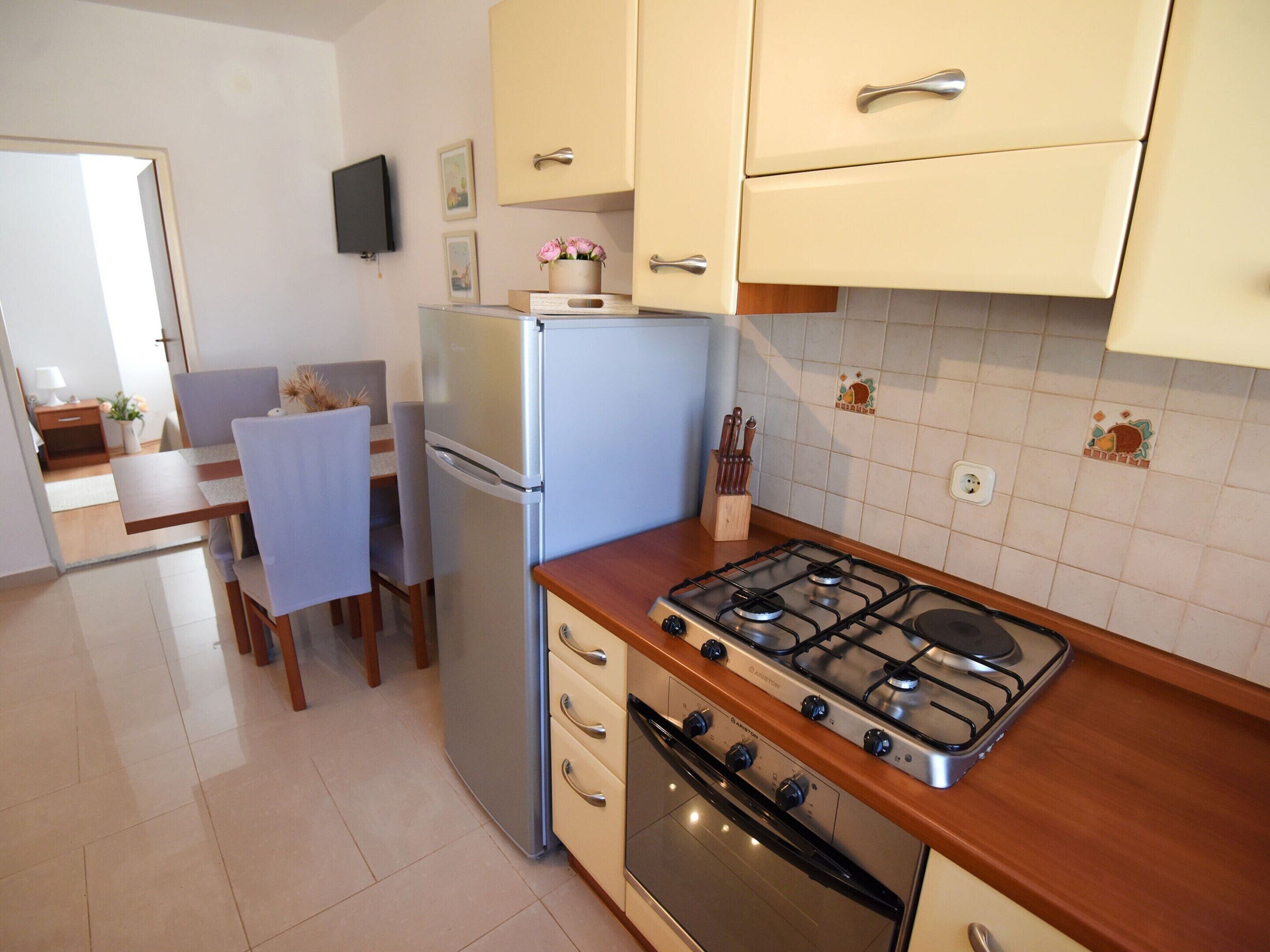 A compact kitchen with a gas stove, oven, refrigerator, and a dining area with chairs and a table.