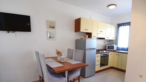 A compact kitchen with a dining area, equipped with a refrigerator, stove, microwave, and a flat-screen TV mounted on the wall. - Apartment in Maslenica Near the Sea (Jasenice)