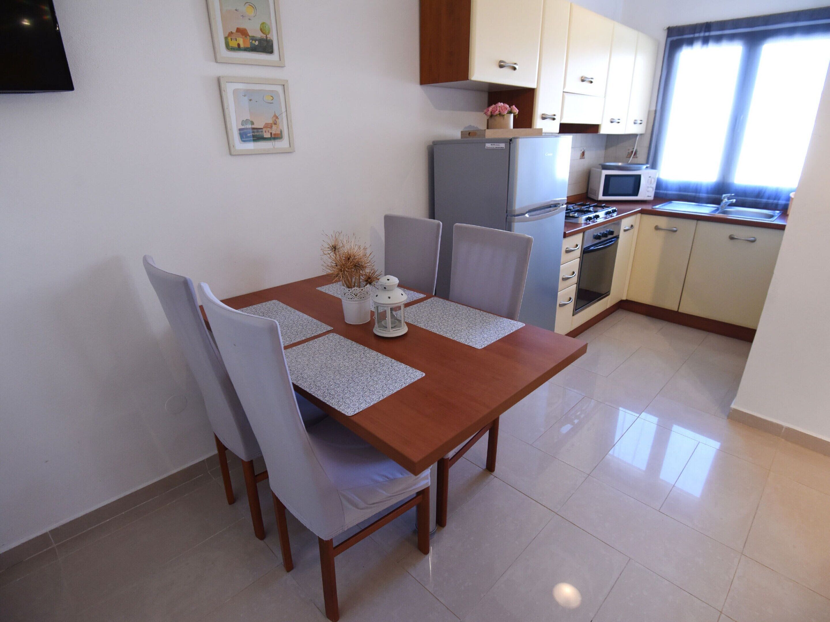 A dining area with a wooden table, four chairs, and a kitchen in the background.
