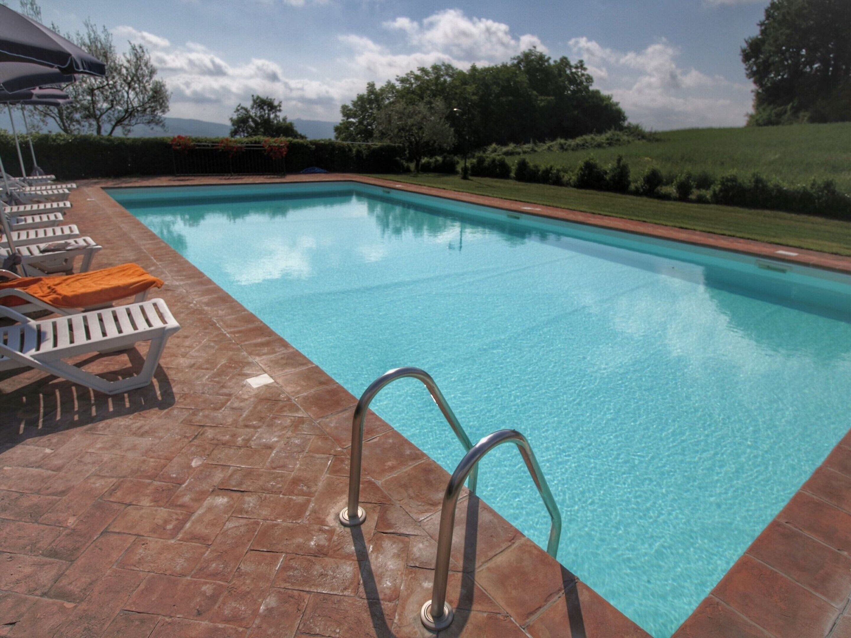 A swimming pool with clear blue water, surrounded by a brick patio and lounge chairs.
