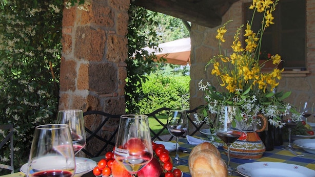 Un espace de restauration en plein air avec une table dressée pour un repas, comprenant des verres à vin, des assiettes de fruits et une miche de pain.