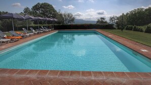 Une piscine rectangulaire bordée de carreaux, entourée d’une terrasse en briques. Des chaises longues et des parasols sont disposés le long du bord de la piscine.