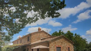 Un bâtiment en pierre doté d’un patio, entouré de verdure et sous un ciel dégagé.