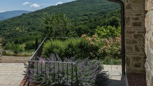 A stone building with a balcony overlooking a lush garden and a mountainous landscape.