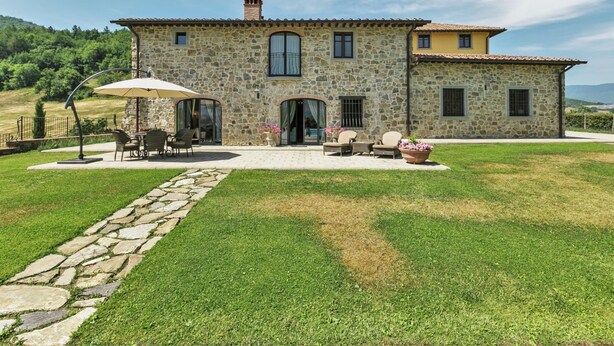 A stone house with a patio, outdoor seating, and a stone pathway leading to the entrance.