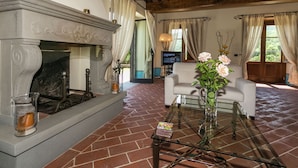 A living room with a fireplace, a glass coffee table, and a TV in the background.