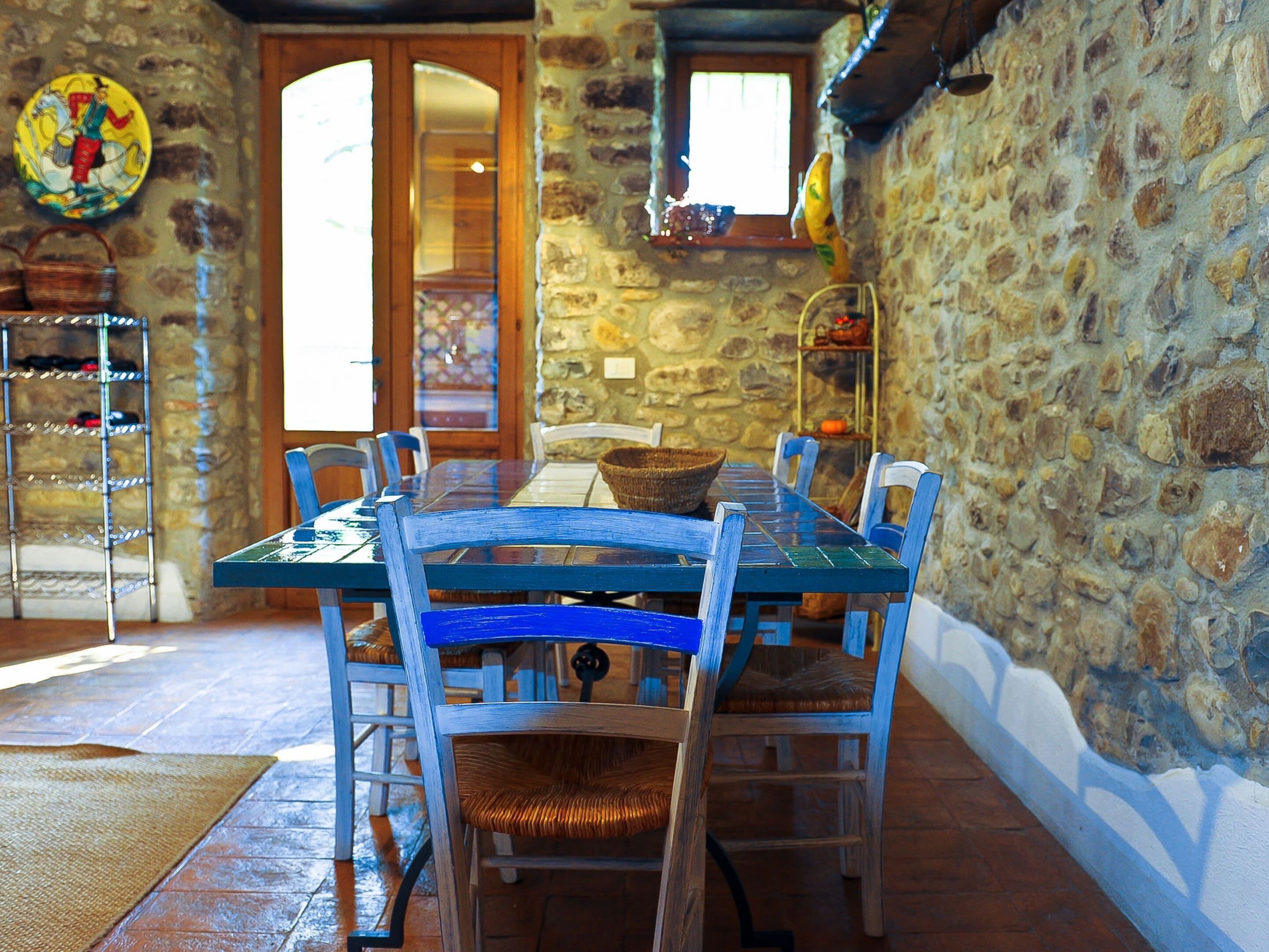 A rustic dining area with a stone wall, a wooden table, and blue chairs.