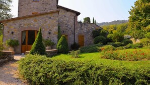 A stone building with a small tower, surrounded by well-maintained hedges and flowering plants.