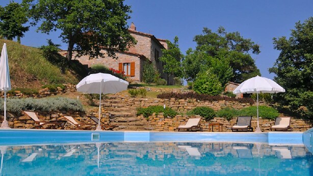 A pool with lounge chairs and umbrellas, surrounded by stone walls and greenery.