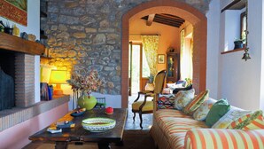 A cozy living room with a stone wall, a fireplace, a wooden table, and a striped sofa.