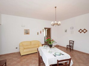 A dining area with a table set for four, a yellow sofa, and a chandelier. - Farmhouse Near Lake Trasimeno With Pool (Passignano sul Trasimeno)