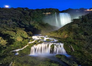 Uma cascata deslizando por um morro verde e coberto por vegetação.