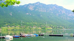 A lakeside view with boats docked, a dock, and a mountainous backdrop. - Apartment in Idro With Pool and Garden (Idro)