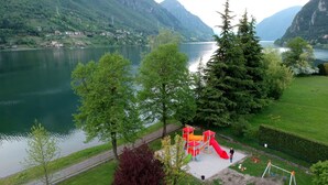 A playground with slides and swings, surrounded by lush greenery and a lake. - Apartment in Idro With Pool and Garden (Idro)