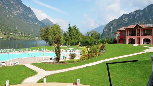 A hotel with a swimming pool, lush greenery, and mountains in the background. - Apartment in Idro With Pool and Garden (Idro)