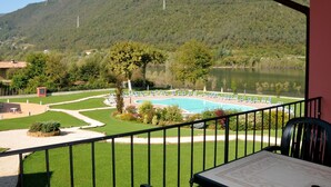 A balcony with a view of a swimming pool, green lawn, and mountains. - Apartment in Idro With Pool and Garden (Idro)
