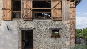 Un edificio rustico con facciata in pietra, persiane di legno e una piccola finestra con fiori.