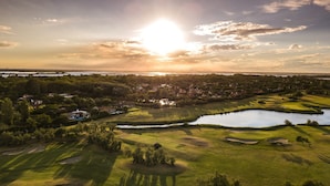 Vista aérea de un campo de golf con un lago, rodeado de zonas residenciales y árboles.