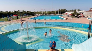 Un área de piscina con varias piscinas, una zona de juegos acuáticos y una solarium para espectadores.
