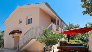A two-story building with a staircase leading to a balcony, a red umbrella, and a wooden bench. - Apartment in Silo With Sea View Balcony (Dobrinj)