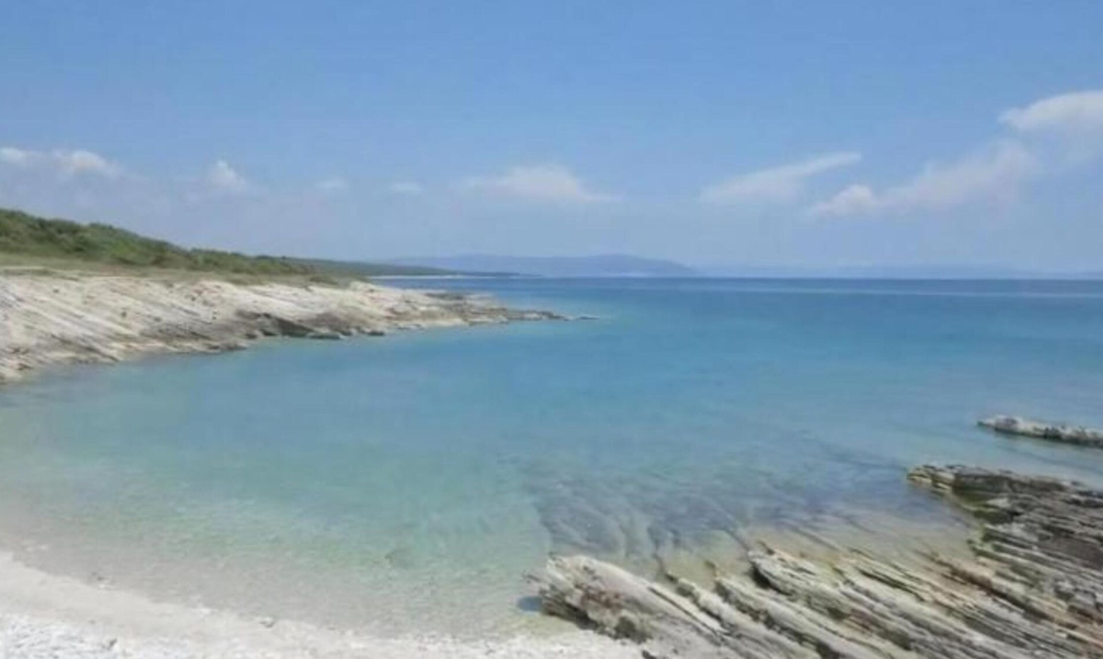 A coastal landscape with clear blue waters and a sandy beach.