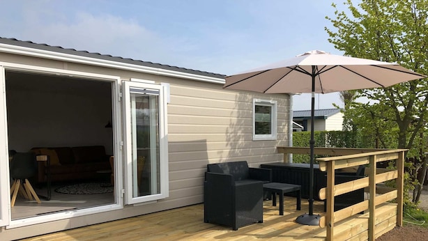 En træterrasse med udendørs møbler og en stor parasol.