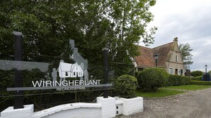 Skilt for WIRINGHERLAND rekreaturpark med silhuet af et hus, omgivet af grøn bevoksning og en bygning med tegltag.