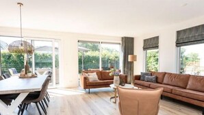 Uma sala de estar moderna com área de jantar, janelas amplas e vista para o verde.