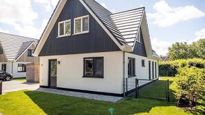 Uma casa moderna de dois andares com telhado escuro, paredes brancas e um pequeno jardim frontal.