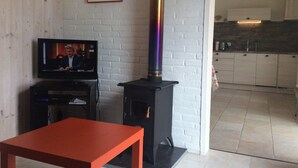 Un salon avec un téléviseur, une table rouge et un poêle à bois noir.
