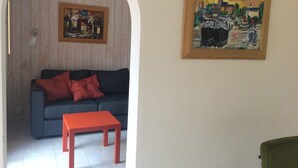 Un salon avec un canapé bleu, des coussins rouges, une table rouge et deux tableaux accrochés au mur.