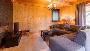 Un intérieur chaleureux, avec des boiseries, un canapé, une table basse, un téléviseur et un lustre.