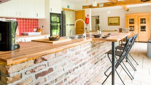 Een keuken met een kookeiland van baksteen, houten kastjes en roestvrijstalen apparatuur, plus een eethoek met stoelen.