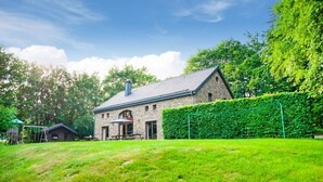 Een gebouw van steen met een schuin dak, een houten terras en een verzorgd gazon.